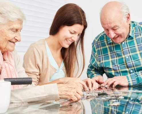 Eine Pflegekraft setzt mit älteren Bewohnern ein Puzzle zusammen