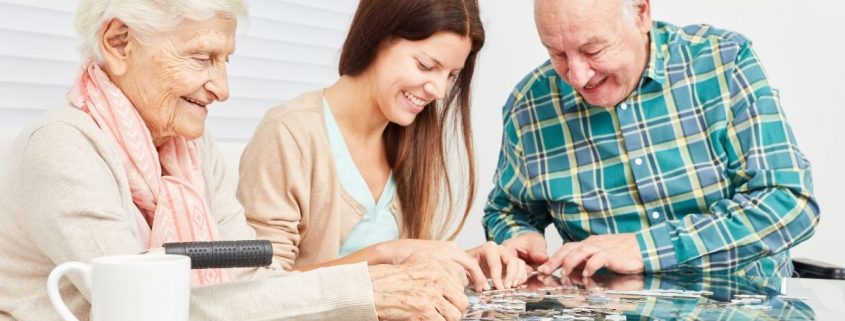 Eine Pflegekraft setzt mit älteren Bewohnern ein Puzzle zusammen